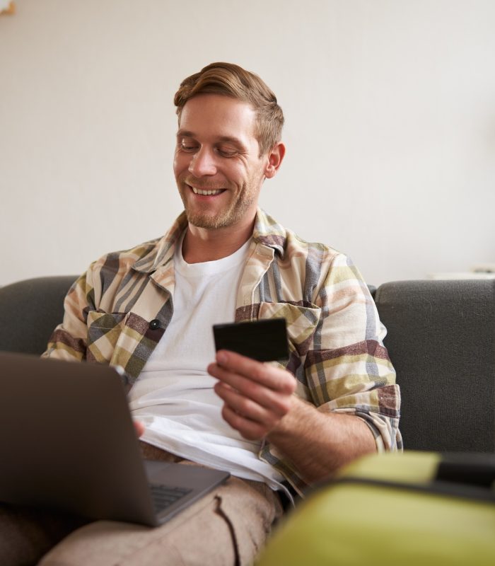 Happy man booking holiday online on laptop, paying for vacation on travel agency website, buying